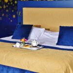 Elegant hotel room with a luxurious breakfast on a blue and gold themed bed.