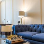 Stylish living room featuring a blue couch, chess set, lamps, and modern decor.