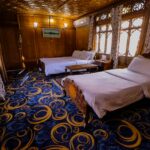 Elegant hotel room with wooden furnishings and twin beds, featuring artistic carpet and curtains for a cozy stay.